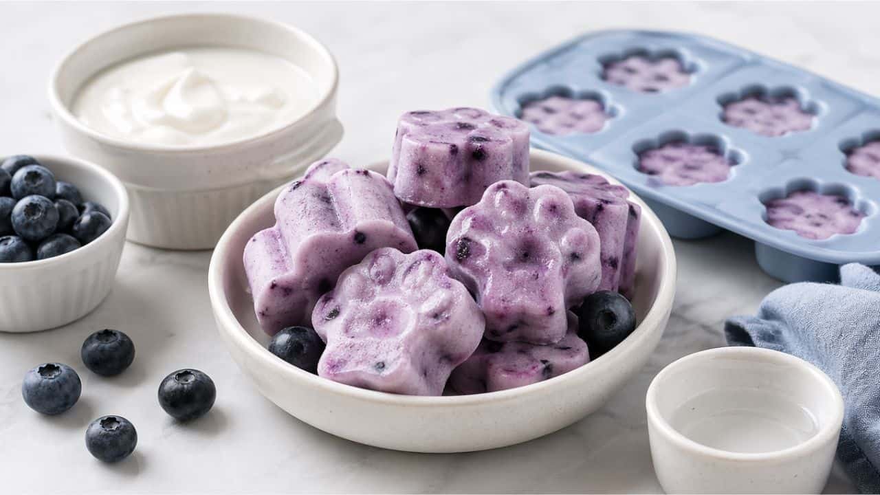 Blueberry yogurt pupsicles in silicone molds with fresh blueberries on a clean marble surface